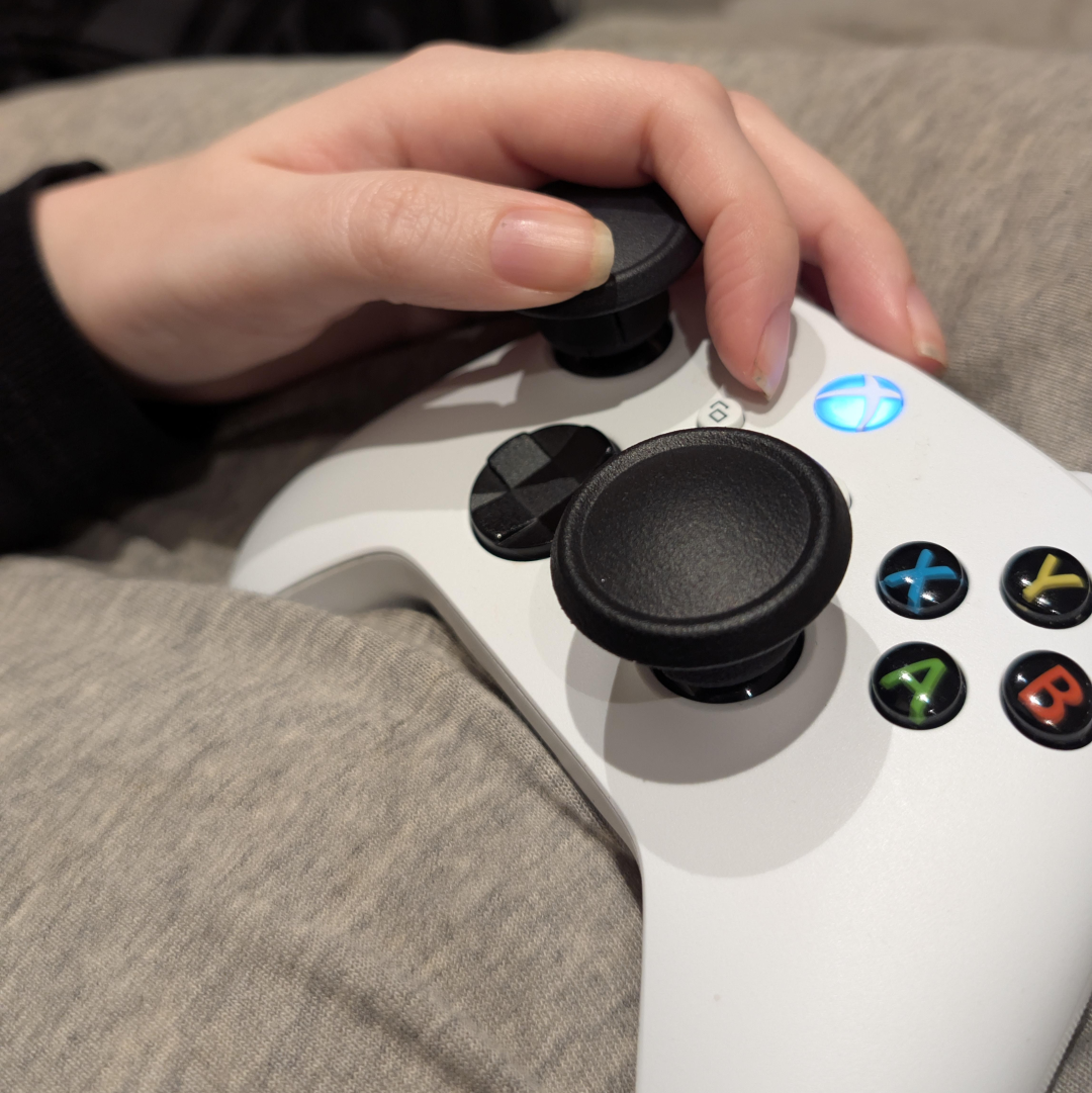 Hand holding a white gaming controller with black buttons on a gray surface