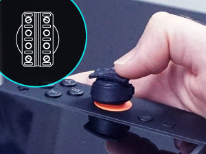 A close-up of a thumb pressing a black thumbstick control on a switch 2 joycon thumbstick gaming controller, with an overlay graphic in the top-left showing a car pedal.