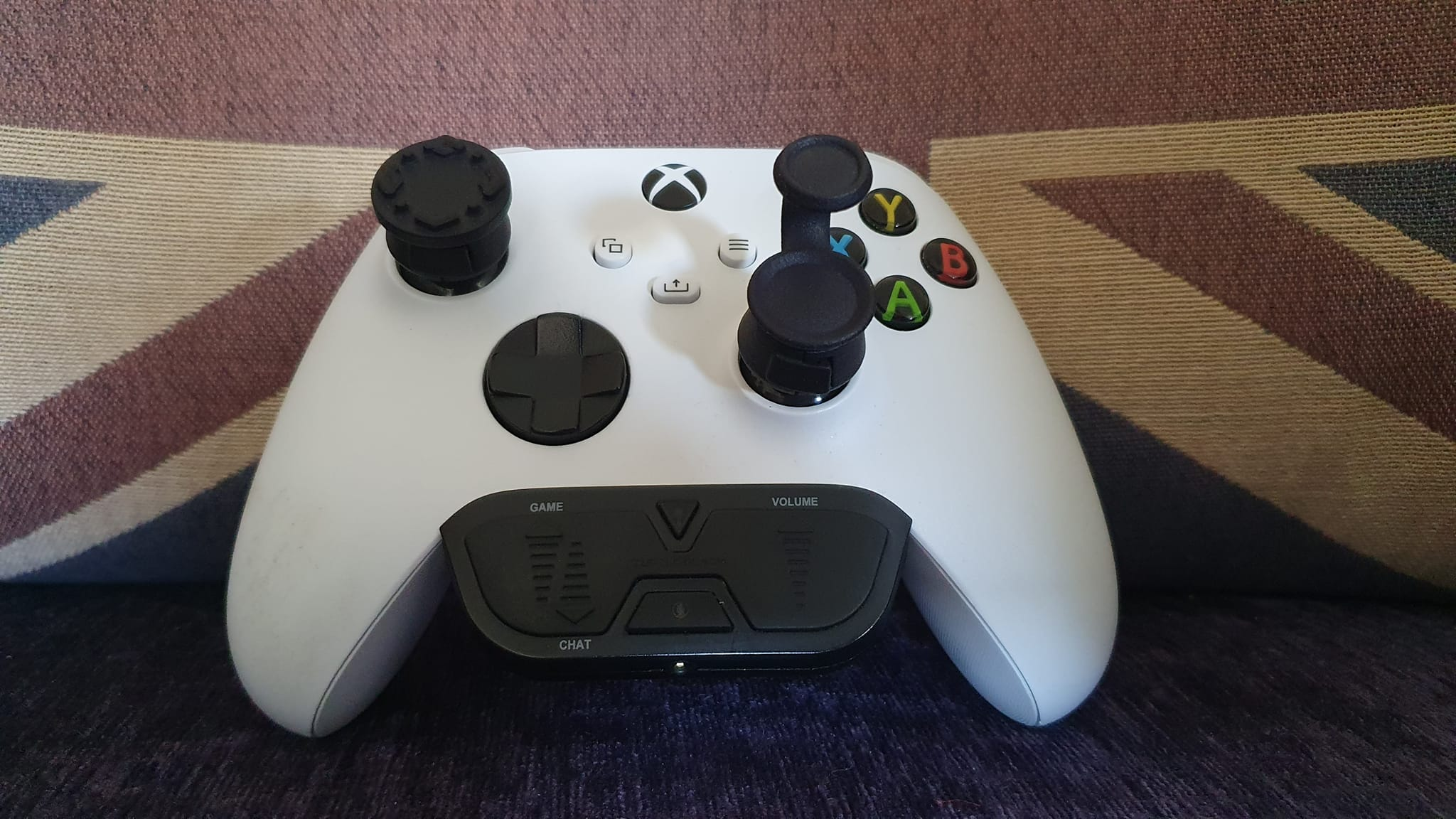 White Xbox controller with Thumb Soldiers Studs thumb grip on left thumbstick and Step Up thumb grip on right thumbstick on union jack mat