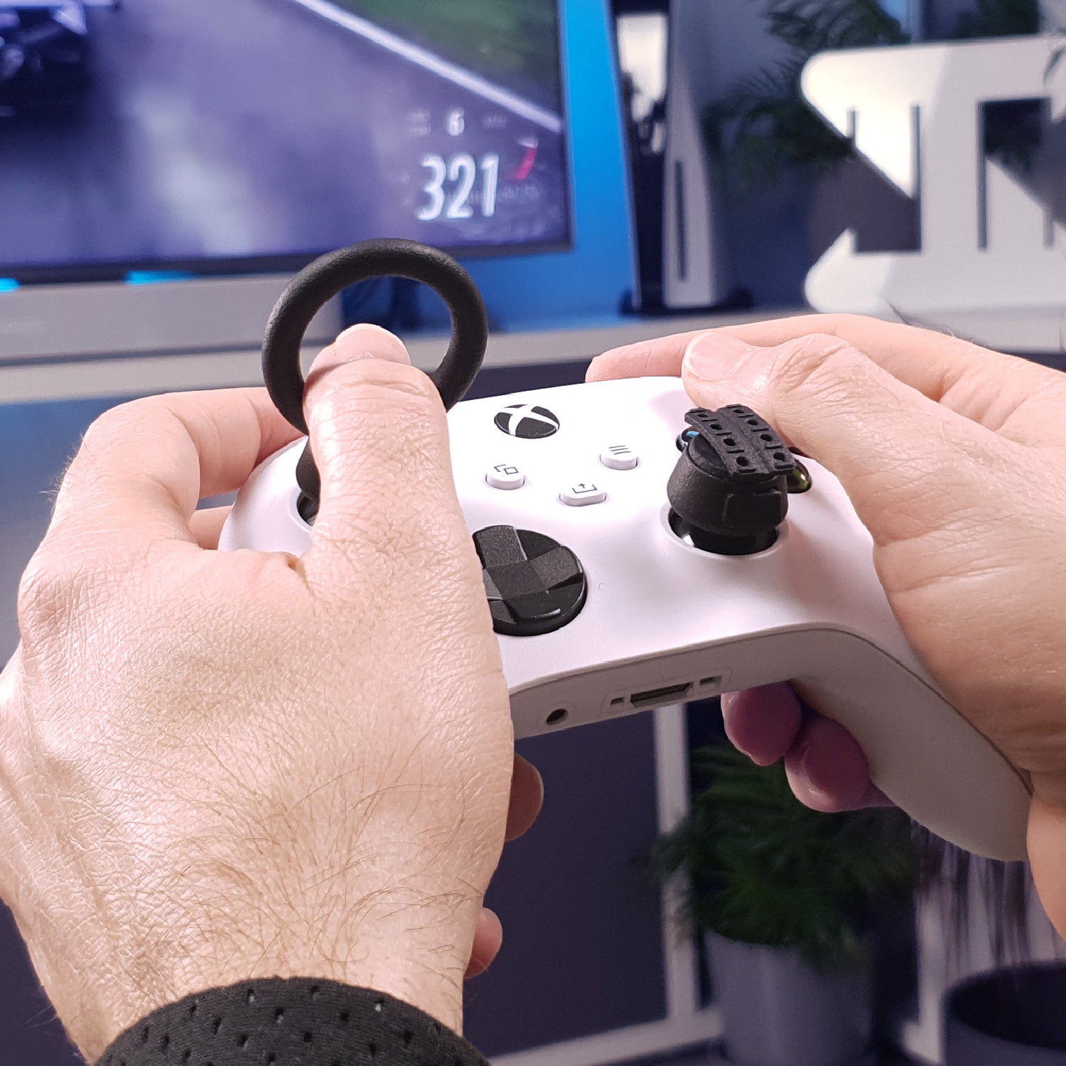 Close-up of hands holding a white gaming controller with Thumb Soldiers Racer kit on and a blurred background