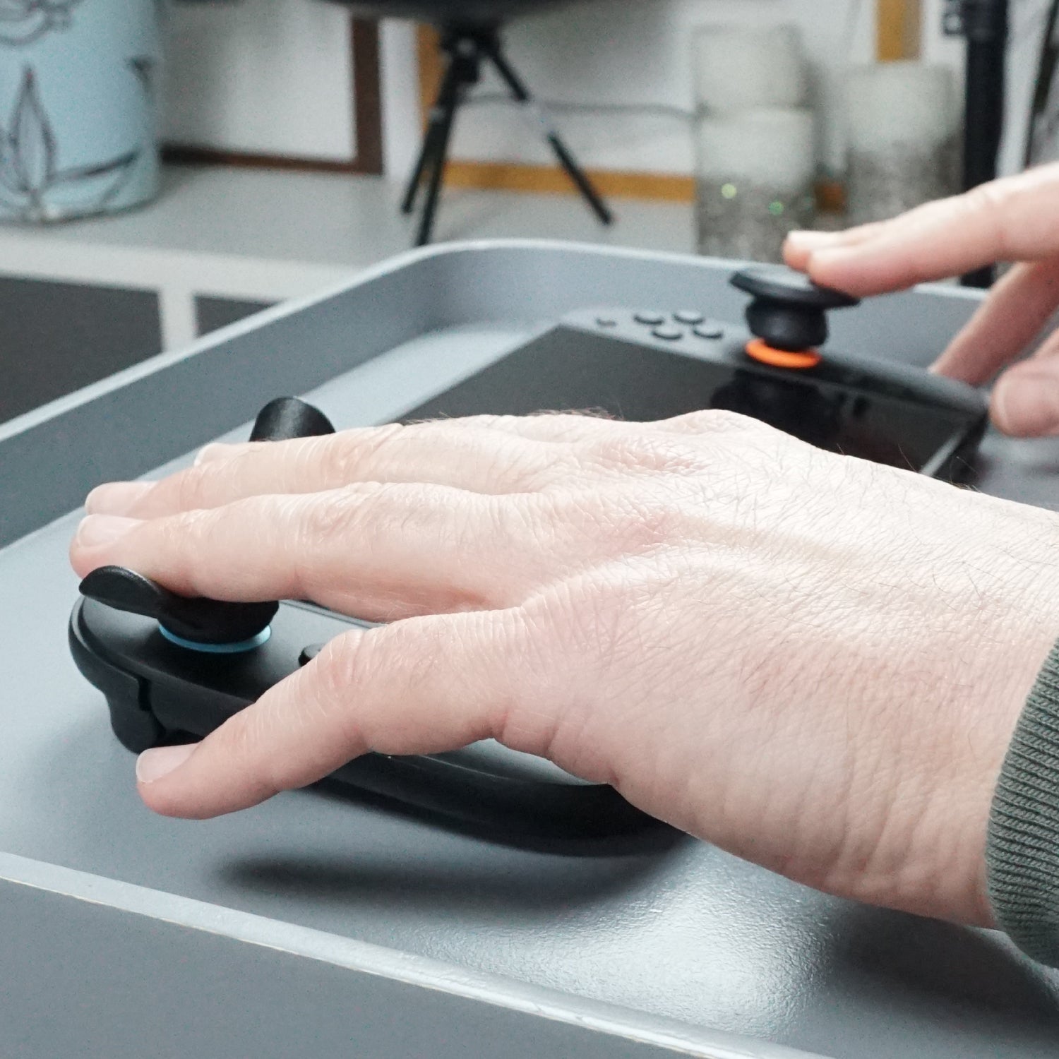 Hand using a gaming controller with Thumb Soldiers Rest kit attachments on a lap tray with a blurred background
