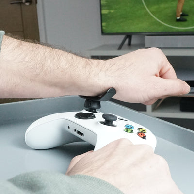 Person holding a white gaming controller with Thumb Soldiers Rest kit attachments and on a desk, with a TV in the background