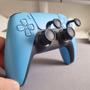 Blue PlayStation controller with Thumb Soldiers' Step Up thumb grips on the thumbsticks, held by a hand on a neutral background