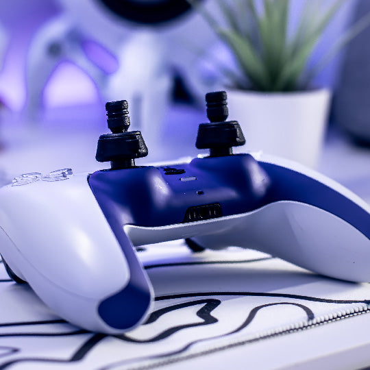 Close-up of a white and blue gaming controller with Thumb Soldiers' Knuckles and Navigation Kits, on a swirly lined mouse mat with a blurred background