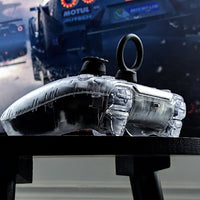 Close-up of a clear Xbox gaming controller with Thumb Soldiers' Knuckles and Racer Kits, with a blurred racing car in the background