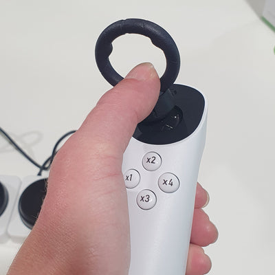 Hand holding a white electronic device with buttons and a black ring, on a blurred background