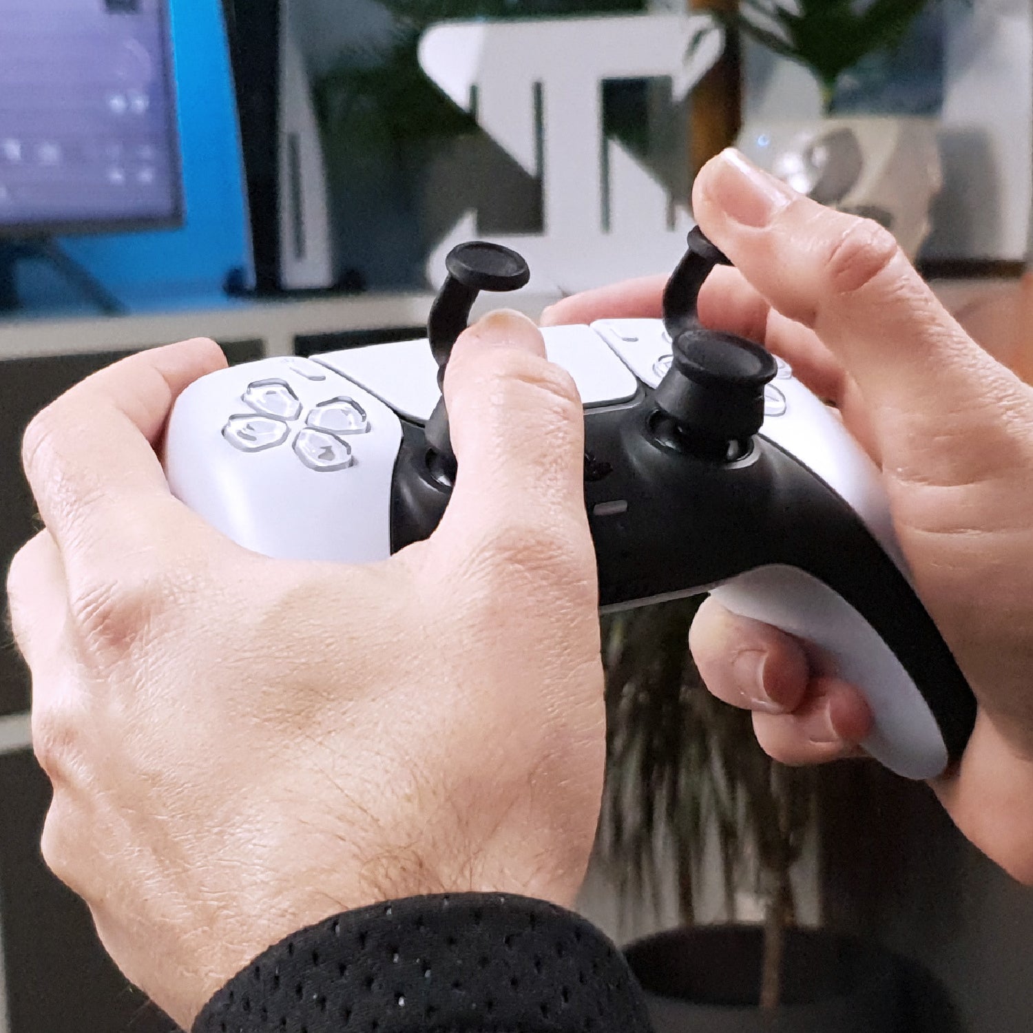 Close-up of hands holding a black and white gaming controller with Thumb Soldiers Step Up attachments in front of a blurred background