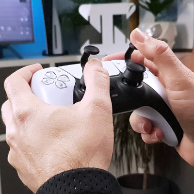 Close-up of hands holding a black and white gaming controller with Thumb Soldiers Step Up attachments in front of a blurred background