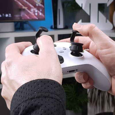 Hands holding a gaming controller with Thumb Soldiers Step Up kit attachments and a blurred background