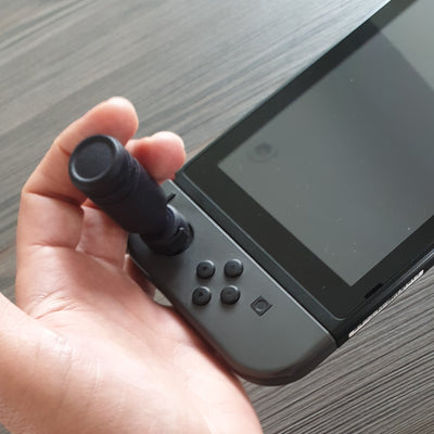 Hand holding a gaming controller with Thumb Soldiers Sticks kit on a wooden surface