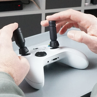 Close-up of hands using a gaming controller with Thumb Soldiers Sticks kit attachments on a desk.