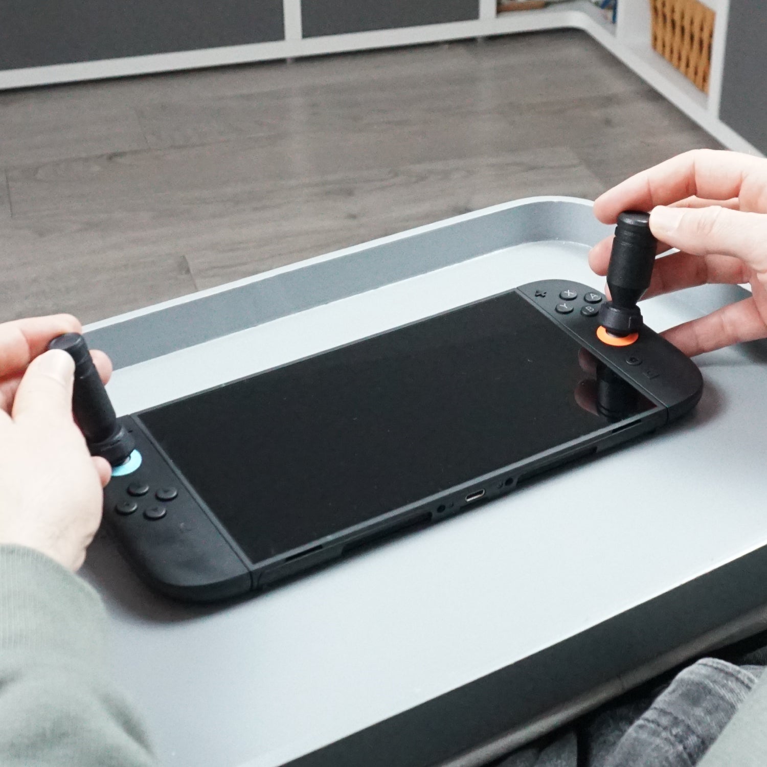 Person holding Switch joycons with Thumb Soldiers Sticks kit attachments on a lap tray.