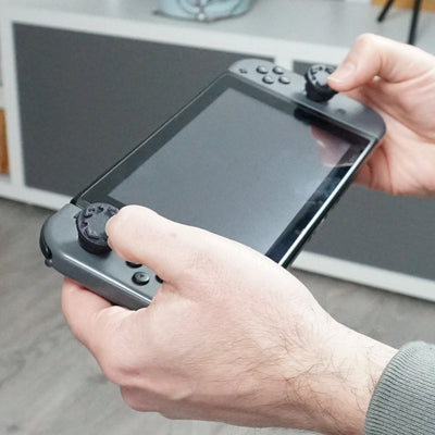 Hands holding a Nintendo Switch console with Studs thumb grips & a blurred background