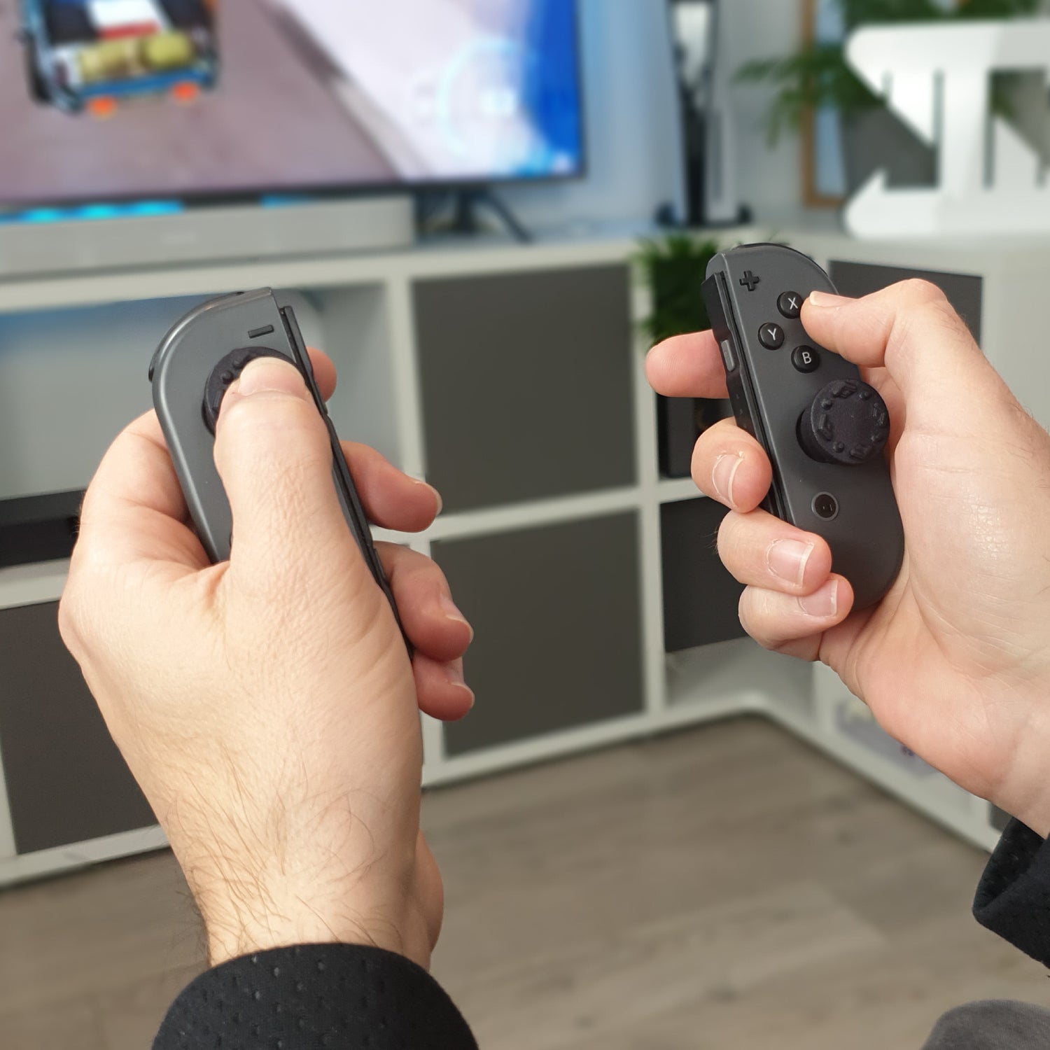 Two hands holding Switch joycon  gaming controllers in front of a television screen.