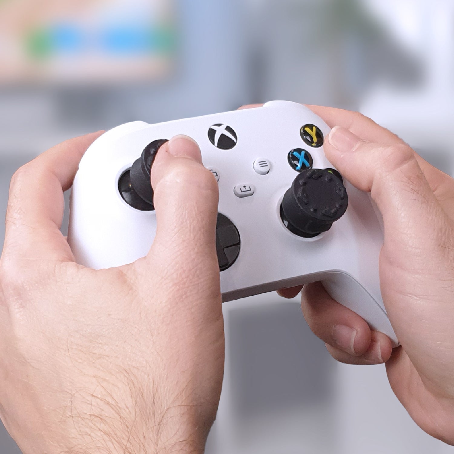 Person holding a white gaming controller with Thumb Soldiers Studs kit on and a blurred background