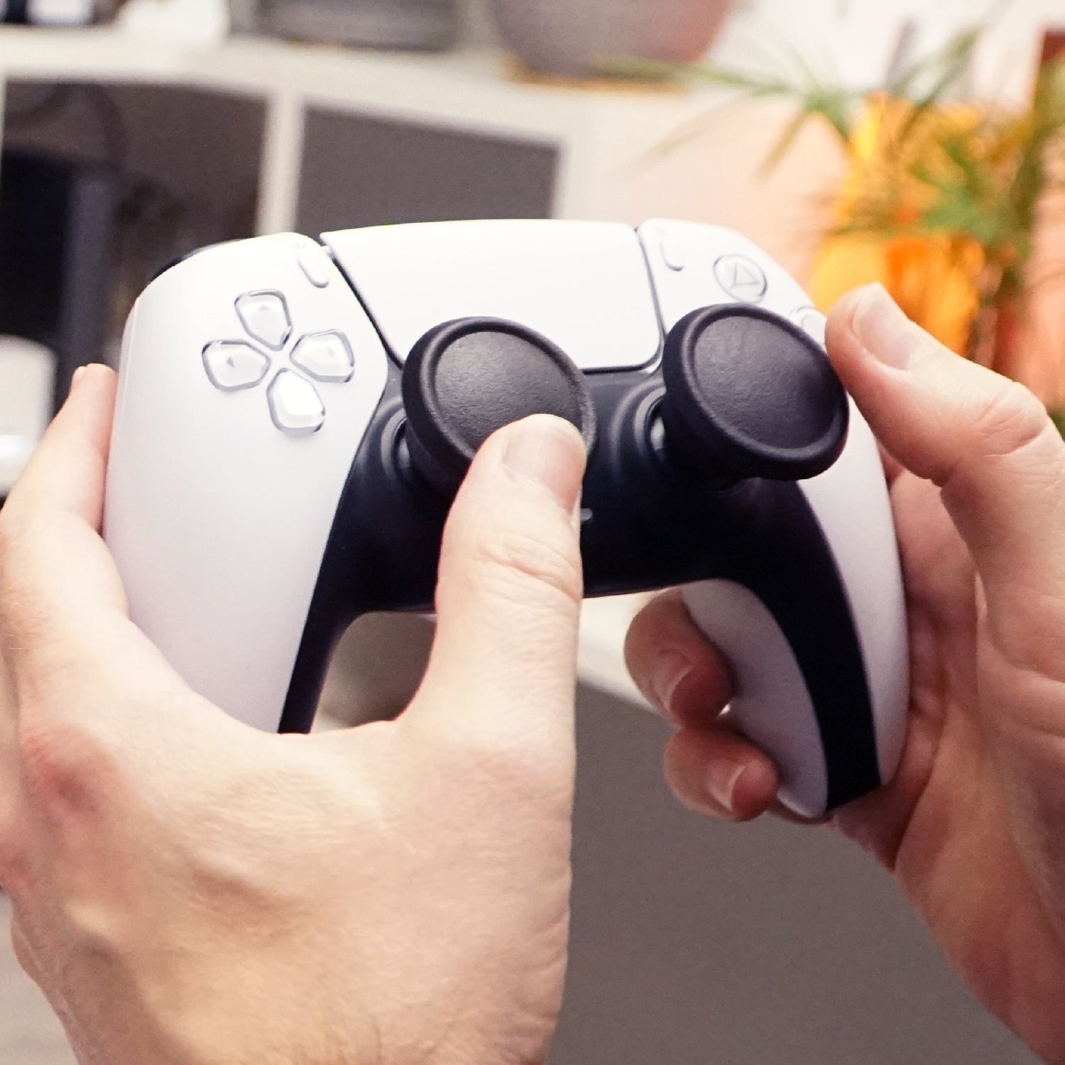 Close-up of hands holding a white gaming controller with Thumb Soldiers Shrooms attachments in front of a blurred background